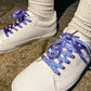 White sneakers with blueberry patterned laces worn on a concrete surface