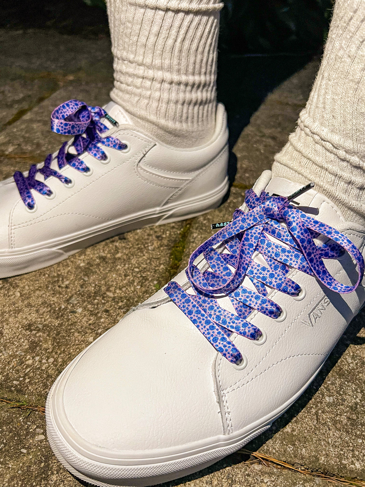 White sneakers with blueberry patterned laces worn on a concrete surface
