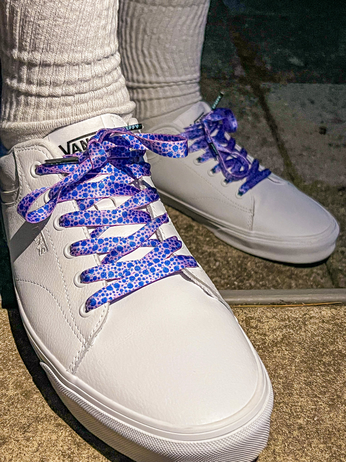 White sneakers with blueberry patterned laces on a concrete surface