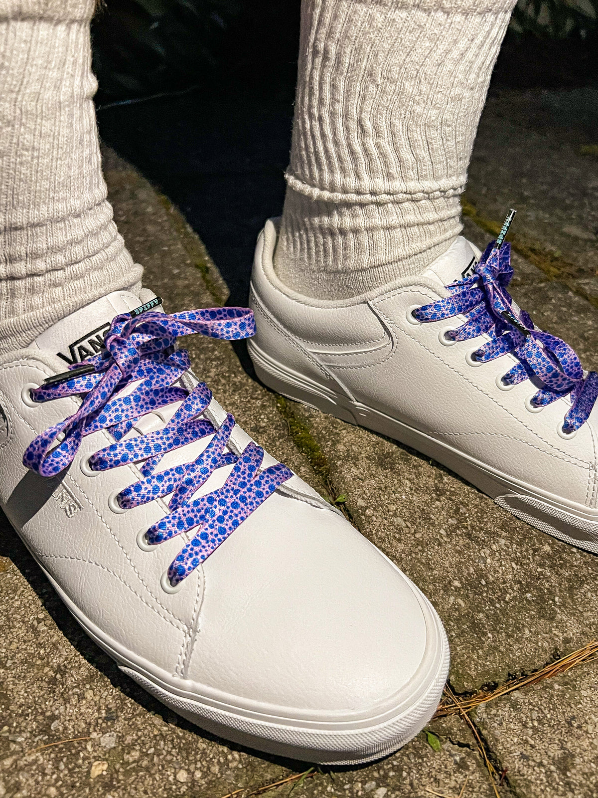 White sneakers with blue patterned laces on a concrete surface