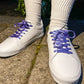 White sneakers with purple laces worn on a concrete surface