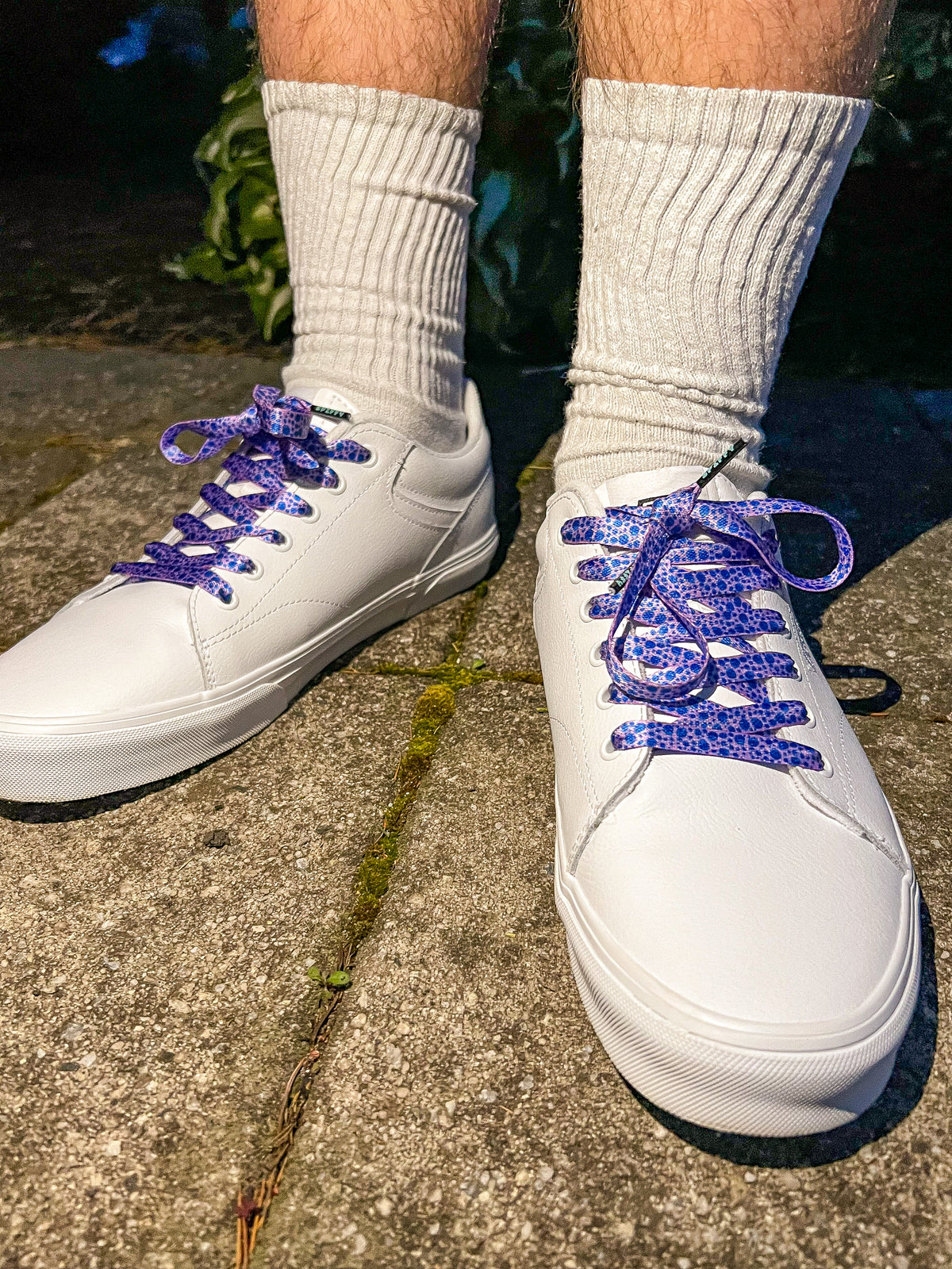 White sneakers with purple laces worn on a concrete surface