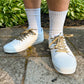 White sneakers with leopard print shoelaces worn on a concrete surface with greenery in the background