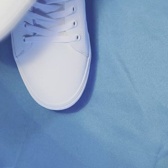 Green and yellow pickle patterned shoelaces being laced up on a fresh pair of white sneakers